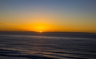 Sonbahar güneşinin yumuşak ışığı kumun dokusunu, dalgaların çizgilerini ve Atlantik 'in sonsuz ufkunu vurgular..