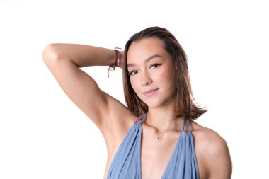 Saçına dokunan genç bir kadının stüdyo portresi mavi bir elbise içinde kendine güvenen ve modern bir görünüm sergiliyor..