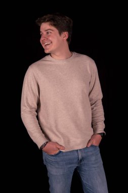 Sıradan kıyafetler giyen genç bir adamın stüdyo portresi. Siyah bir arka plana bakarken doğal bir şekilde gülümsüyor. Görüntü güven, pozitiflik, özgünlük ve rahat bir yaşam tarzı iletir..