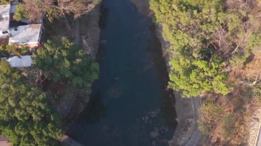 Günbatımında Cuernavaca 'daki Chapultepec Parkı' nda yaşanan kuraklıktan etkilenen bir nehrin üzerinden geçen sinematik dron, düşük su seviyesi, sıcak akşam ışığı ve kentsel park üzerindeki iklim değişikliğinin görünür etkisini vurguluyor.