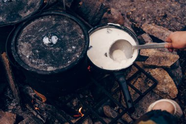 Kamp ateşi mutfağında piknik yapan turist, metal tabağa kremalı çorba koyar.