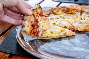 Pizzacıya gelen ziyaretçi elinde İtalyan Margherita pizzasından bir dilim tutuyor.