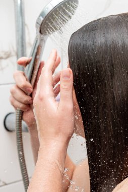 Duştaki genç kadın, uzun saçlarını şampuanla, özenle ve sıhhatle yıkayan kişi.