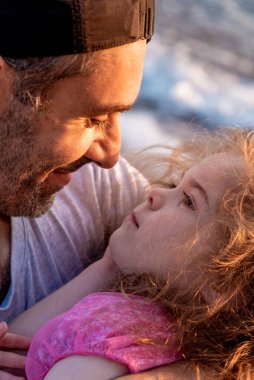 Aile babası ve kızı yaz tatilinde sahilde yürüyor.