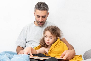 Aile babası ve kız çocuk kitabı okuyor, baba yatmadan önce kızına hikaye anlatıyor.