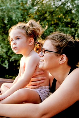 Uzağa bakan anne ve kızın portresi. Küçük kıza sarılan kadın.