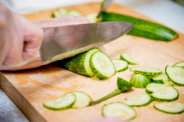 Mutfaktaki restoranda aşçı sebze salatası hazırlıyor, yakın çekimde domates ve salatalık kesiyor.