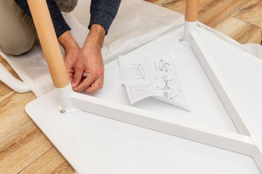 Tamirci adam yeni ahşap yemek masasını tornavida ve vidayla birleştiriyor.