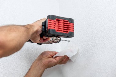 Tamirci adam duvarda matkapla delik açıyor, inşaat malzemeleriyle evde tamirat yapıyor.