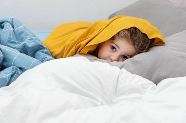 Sevimli küçük kız yastık portresi üzerinde yatakta yatıyor, çocuk yatmadan önce oynaşıyor.