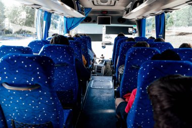 İnsanlar güneşli bir yaz gününde, büyük bir şehir otobüsünde, pencerenin önünde mavi sandalyelerde otururlar.