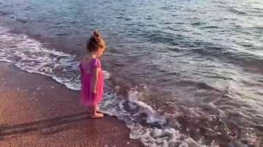 Kıyıdaki gölette sarı kum ve deniz dalgalarıyla oynayan tatlı bir kız.