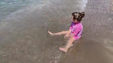 Kıyıdaki gölette sarı kum ve deniz dalgalarıyla oynayan tatlı bir kız.