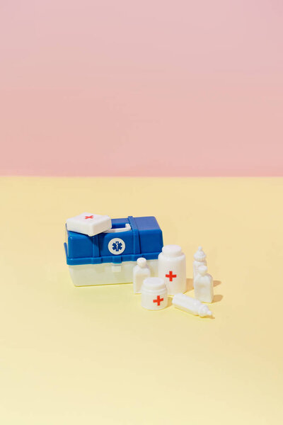 Toy medical suitcase with veterinary medicines and instruments on pink and yellow background creative composition