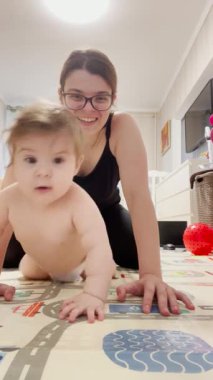 Küçük tatlı kız yerde sürünmeyi öğreniyor, annesi gülümsüyor ve kızını izliyor.