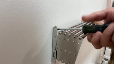 Man repairman screw hand screwdriver and installs folding clothes dryer on the wall