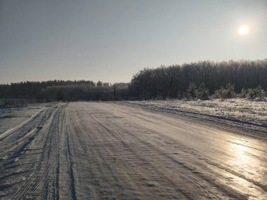 Kış manzarası boyunca ufukta orman olan buzlu kırsal yol. Soğuk hava ulaşım arkaplanı.