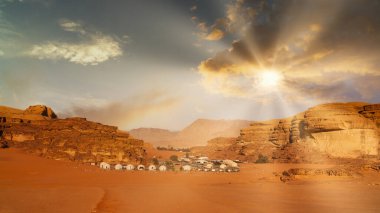 Wadi Rum Çölü, Ürdün, Ay Vadisi. Gün batımında bir grup çadır çöl manzarasına kurulur. Güneş kumlu araziye ve kaya oluşumlarına ışık saçıyor..