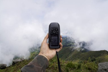 Bir yürüyüş macerası sırasında sisli bir dağ manzarasına karşı el bilgisayarlı GPS cihazı..