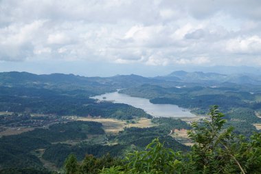 Serin bir gölün panoramik görüntüsü bulutlu bir gökyüzünün altındaki yemyeşil dağlarda süzülüyor..