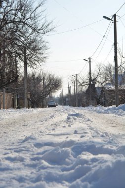 Güneşli bir kış gününde, tekerlek izleri olan köydeki karlı bir yolun alçak açısı.