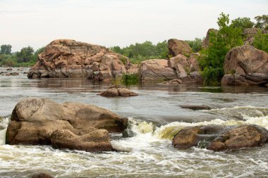Yeşil bitki örtüsüyle çevrili kayalık nehir manzarası ve taştan oluşumlar. Nehir akıntılı doğal manzara ve sakin açık hava atmosferi.