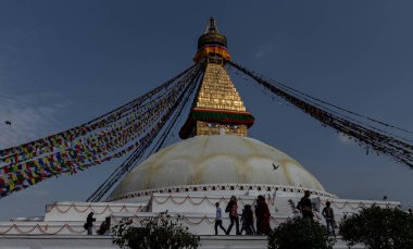 Katmandu, Nepal 8 Mart 2015: Boudhanath Stupa 'da akşam duası bayrakları ve aydınlatılmış altın kuleyle yürüyen ziyaretçiler.