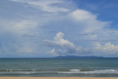 Yumuşak dalgalar ön plandaki kumlu bir sahile doğru yuvarlanarak yumuşak, ritmik bir doku oluşturur. Uzakta, ufukta bir kara parçası ya da ada yükselir ve kompozisyona derinlik ve denge ekler..