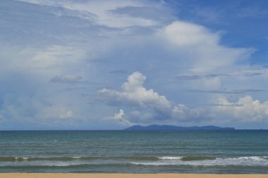 Mavi gökyüzünün altında, dağınık bulutlarla sakin bir okyanus.