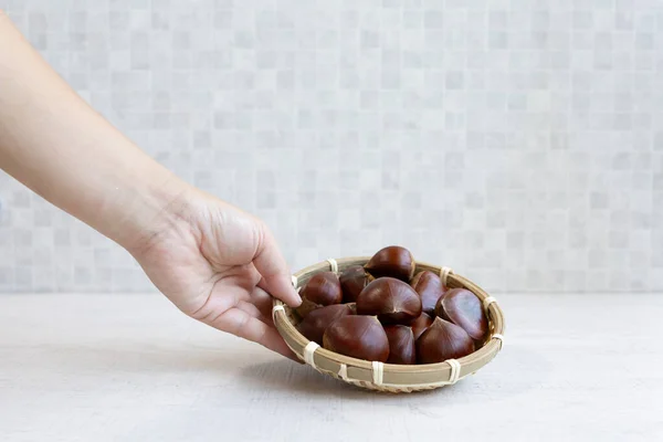 Elin beyaz masada taze kestane dolu bambu sepetini tutuyor.
