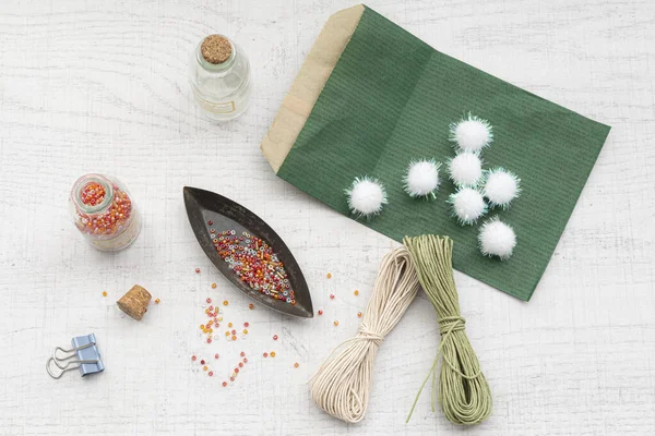 Boncukları, ponponları ve beyaz bir masada ipi olan el sanatları malzemeleri.