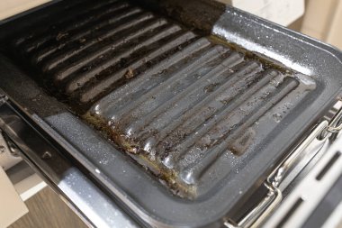 Eti pişirdikten sonra fırının içinde kirli, yağlı ızgara tepsisi yakın plan.