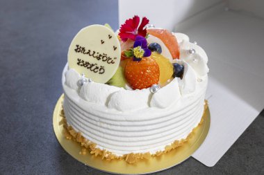 Meyveli, kremalı ve Japonca tebrik mesajlı doğum günü pastası.