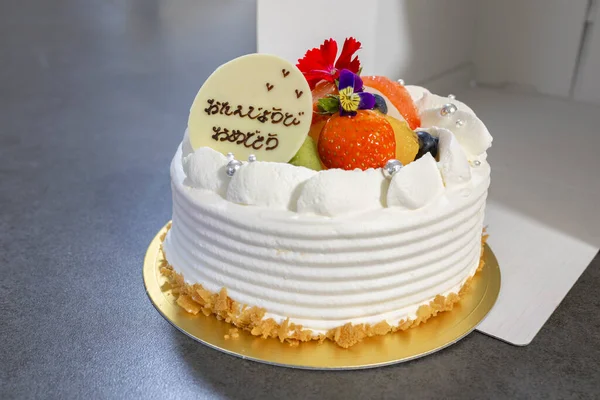 Taze meyve ve yenilebilir çiçeklerle süslenmiş beyaz doğum günü pastası.