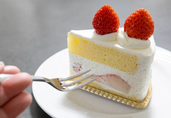 Çatallı el çilekli pasta diliminden bir ısırık almak üzere.