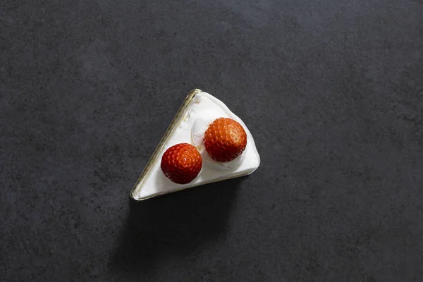 Koyu bir masada üçgen bir çilekli pasta diliminin üst görüntüsü.