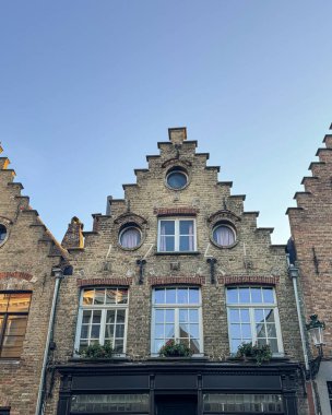 Geleneksel Flamanlar, açık bir gökyüzü altında yakalanan geniş pencereli ve çiçek kutulı basamaklı tuğla evler. Klasik Avrupa mimarisi ve tarihi cazibesi huzur dolu eski kasaba sokaklarında.