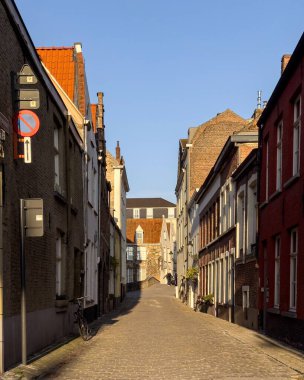 Bruges, Belçika 26 Aralık 2025. Soğuk bir kış sabahı, Bruges 'ün tarihi merkezinde sakin bir kaldırım taşı caddesi. Geleneksel tuğla konaklar dar bir sokakta, yumuşak güneş ışığı cepheleriyle yan yana diziliyor..