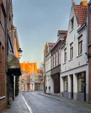 Bruges, Belçika, 26 Aralık 2025. Tarihi merkezin sessiz kıvrımlı caddesinde kışın gökyüzünün altında beyazlatılmış ve tuğladan evler var. Güneş ışığı, geleneksel Flaman binalarının çatılarına vurarak, Avrupa mirasının davetkar bir sahnesini yaratıyor..