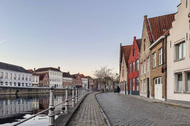 Bruges, Belçika, 26 Aralık 2025. Bruges 'deki Cobblestone Kanal sokağı tarihi basamaklı evler ve renkli cephelerle doludur. Sakin akşam ışığı suyu yansıtır, eski kasabanın atmosferini yakalar..