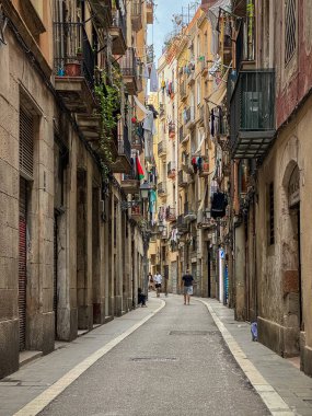 Barselona, İspanya 2 Ekim 2025: Balkonları, panjurları ve asılı çamaşırları olan yüksek binalarla çevrili kıvrımlı ortaçağ caddesi, Barselona, Katalonya 'nın tarihi merkezinde otantik mimari ve günlük yaşamı gösteriyor.