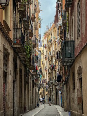 Barselona, İspanya 2 Ekim 2025: Taş cepheli, balkonlu, dükkan önlü ve yürüyen insanların bulunduğu atmosferik eski kasaba sokak sahnesi. Barcelona, Ciutat Vella bölgesinde seyahat ve şehir yaşam tarzı.