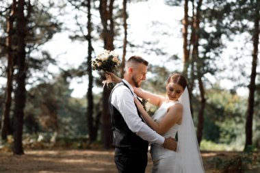 Bir çift ormanda bir arada durur, gülümseyerek ve düğünleri boyunca birbirlerine eşlik ederek eğlenirler. Damat bir buket tutarken gelin ona sevgiyle bakar..