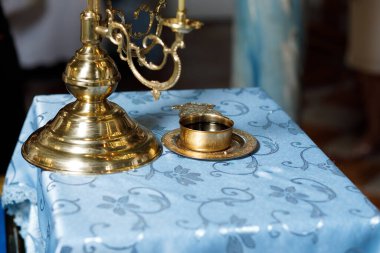 Bir mum tutacağı mavi bir bezle bir masanın üzerinde dimdik durur. Yanında küçük bir tabakta metal bir kupa duruyor. İnsanlar sosyal bir etkinlik için yakınlarda toplanıyor, canlı bir atmosfer yaratıyorlar..