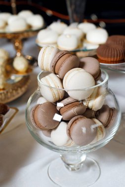 Cam bir kase, bir toplantıda tatlı sergisi sırasında farklı renklerde makarna içerir. Ayarda yakınlardaki masalarda başka ikramlar da yer alıyor.