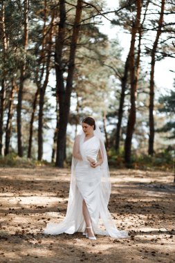 Uzun beyaz bir elbise ve duvak takmış bir gelin ormanda yürüyor. Bir buket tutuyor ve güneşli bir günde etrafını saran uzun ağaçlar gibi gülümsüyor. Güneş ışığı yaprakların arasından süzülür..