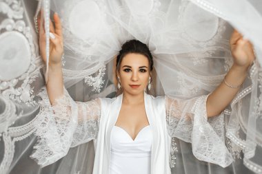 Bir gelin, elinde narin bir peçeyle düğün elbisesiyle hazır bekliyor. Ayar çok parlak ve yaklaşan törene odaklanmış durumda. Neşeli ve heyecanlı..