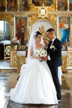 Çift kilisede dururken resmi kıyafetler giyer. Bir buket tutarlar ve birbirlerine bakarlar. Dekor, arka planda dini simgeler ve dekorasyonları içeriyor.