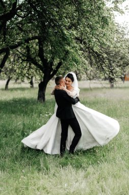 Bir çift, ağaçlarla dolu çimenli bir alanda düğünlerinin tadını çıkarıyor. Kadın beyaz bir elbise giyiyor ve erkek koyu bir takım elbise giyiyor. Bu anda sevinçleri açık..