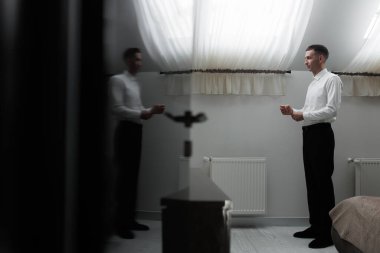 Parlak odada beyaz gömlekli bir adam var, aynanın karşısında duruyor, sabahları pencereden süzülen hafif ışık gibi kendini yansıtıyor..